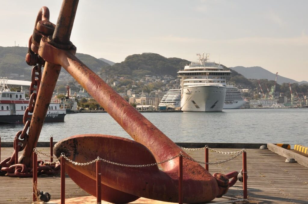 歴史を感じさせる大きな錨の向こうに現代の豪華客船シーボーン・アンコールを望む
