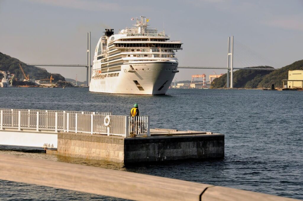 長崎港へ真っ直ぐに進むシーボーン・アンコールと桟橋から見守る作業員の背中